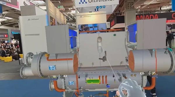 POV of a trade fair visitor using AR glasses and hand-tracking to manipulate a high-poly digital twin of an industrial cooling machine on a crowded exhibition floor.